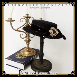 Gothic lolita flat bonnet with black velvet bow and ornate gold heart brooch, displayed on vintage tabletop with candlestick and antique book, front oblique angle