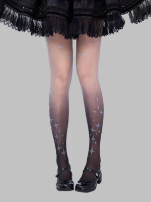 Front full-leg view of gradient black-to-skin-tone Gothic Lolita pantyhose with four-point silver star prints, styled with black ruffled Lolita skirt and Mary Jane shoes against plain background