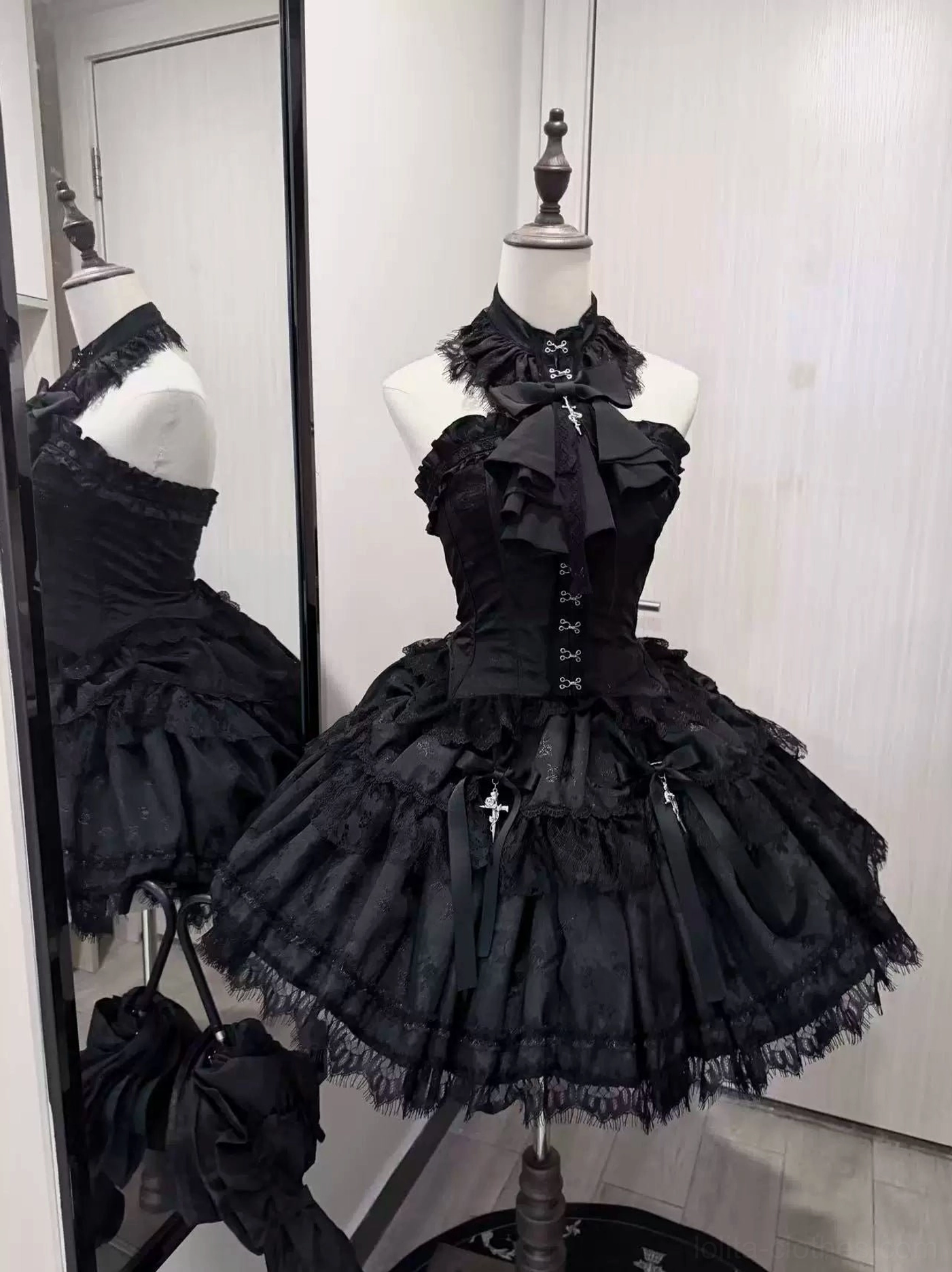 Black halter neck gothic lolita corset with cross front closures and layered mesh skirt with cross charms and lace trim, front three-quarter view studio mannequin display