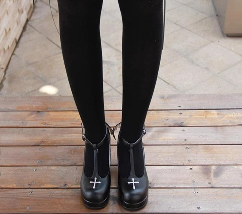 On-foot wearing demonstration of Gothic Lolita high heel shoes with cross embroidery, front low-angle view showing shoes with black tights, outdoor wooden terrace scene setting