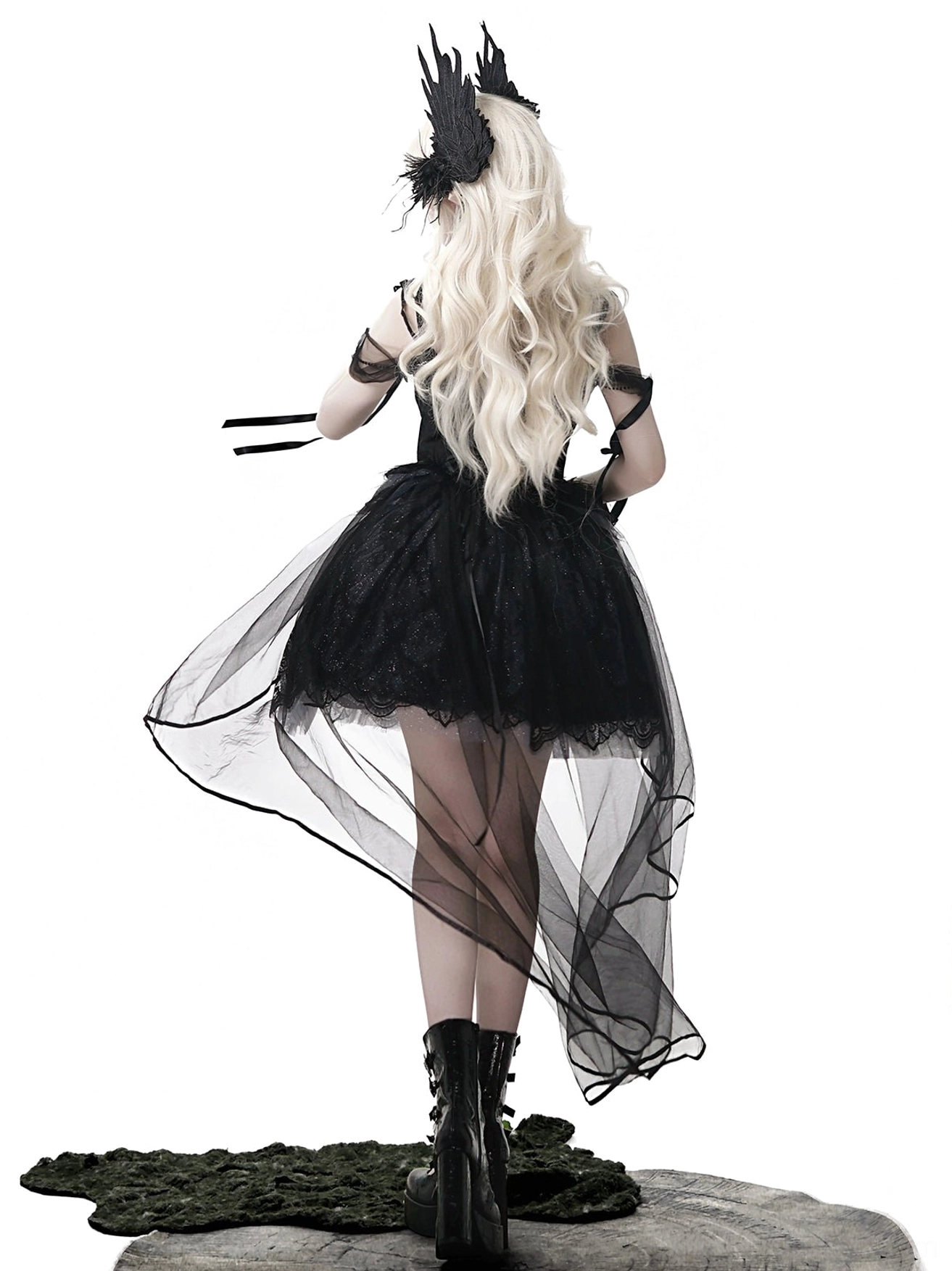 Black gothic lolita JSK dress full back view on model with long blonde hair and black feather gothic headpiece, showing sheer high-low tulle train and form-fitting lace bodice with open-back straps