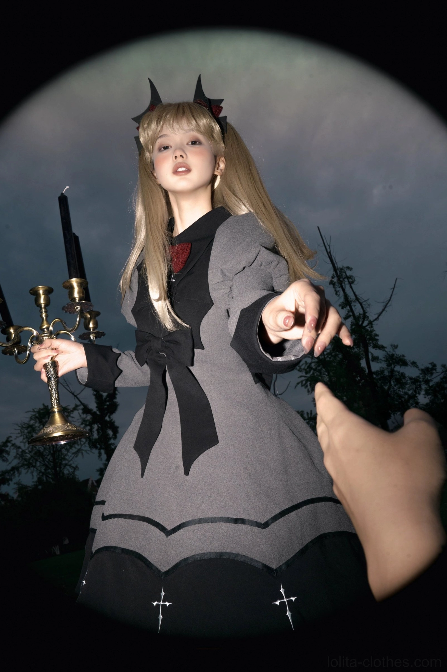 Bat-inspired gothic lolita OP dress front low angle shot model in dark forest with candelabra prop devil horn accessories