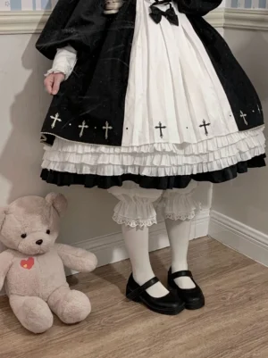 Gothic lolita complete outfit coordination featuring cross-print op dress white lace-trimmed bloomers peeking from hem white stockings and black mary jane flats standing beside teddy bear prop