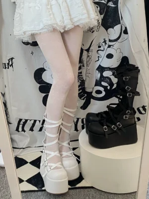 Overhead mirror view of gothic lolita platform shoes and boots displayed on checkered floor, model wearing white ruffled mini skirt with dotted stockings, showcasing dual-color crisscross buckle strap design