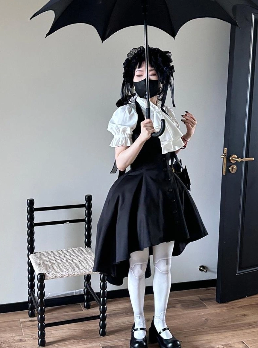 Full-body Gothic Lolita coordinate featuring white ruffled short-sleeve blouse with black asymmetrical high-low skirt, white stockings and gothic Mary Jane shoes on model in indoor scene