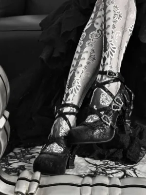 Gothic lolita skeleton heel pumps worn with lace stockings and dark clothing on patterned gothic surface close-up view