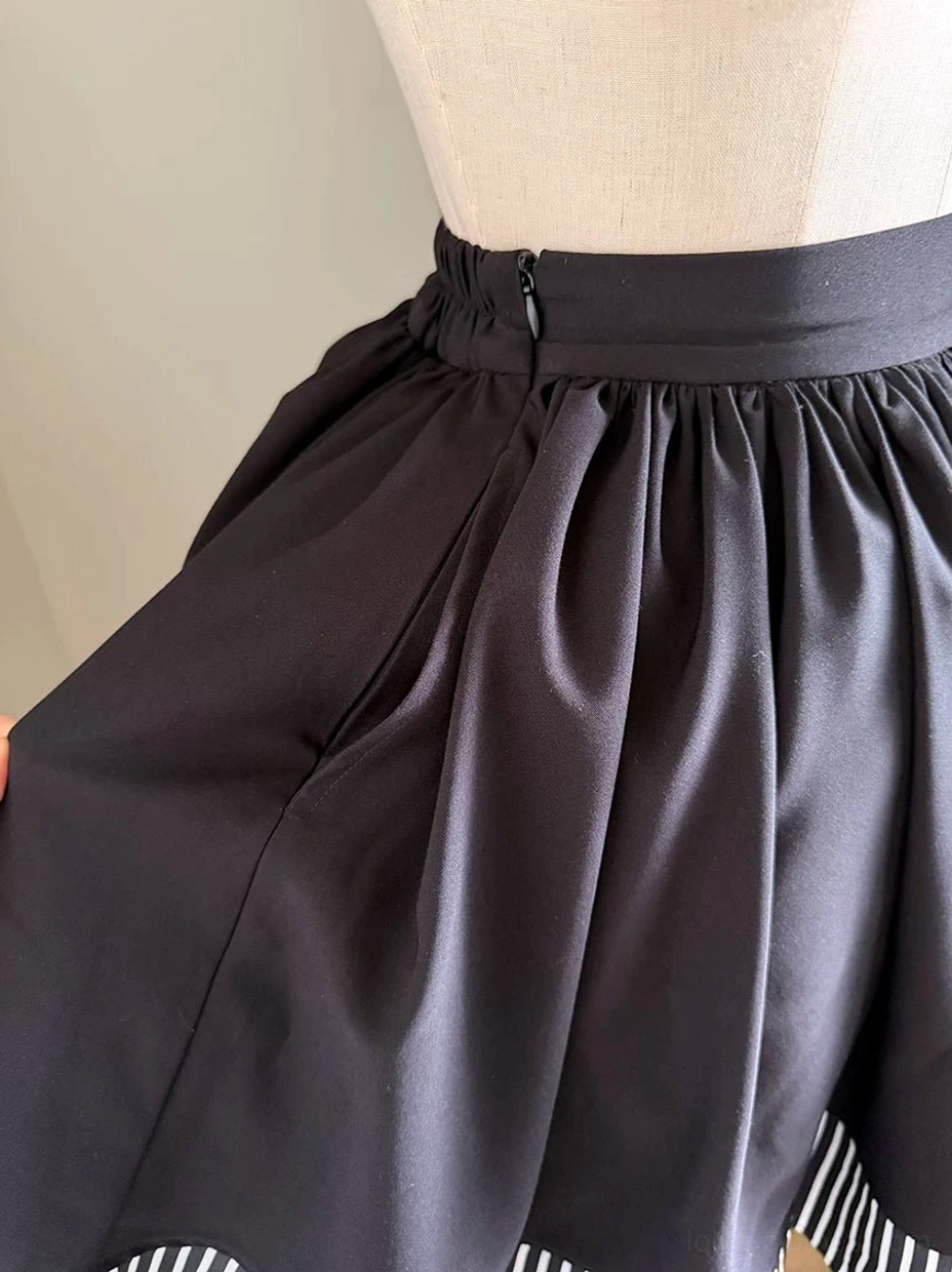 Close-up side view gothic lolita skirt showing hidden side zipper closure smooth black woven fabric gathered pleats striped ruffled hem detail