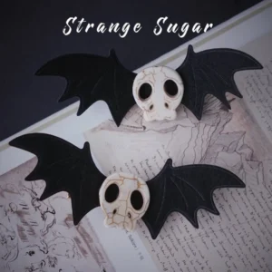 Gothic lolita skull and bat hair clips pair displayed on vintage handwritten paper background showing black fabric bat wings and off-white skull ornaments
