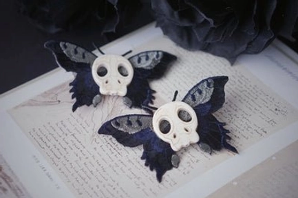Skull moth lolita hair clips pair black moth wings with off-white skull ornament on vintage handwritten document background