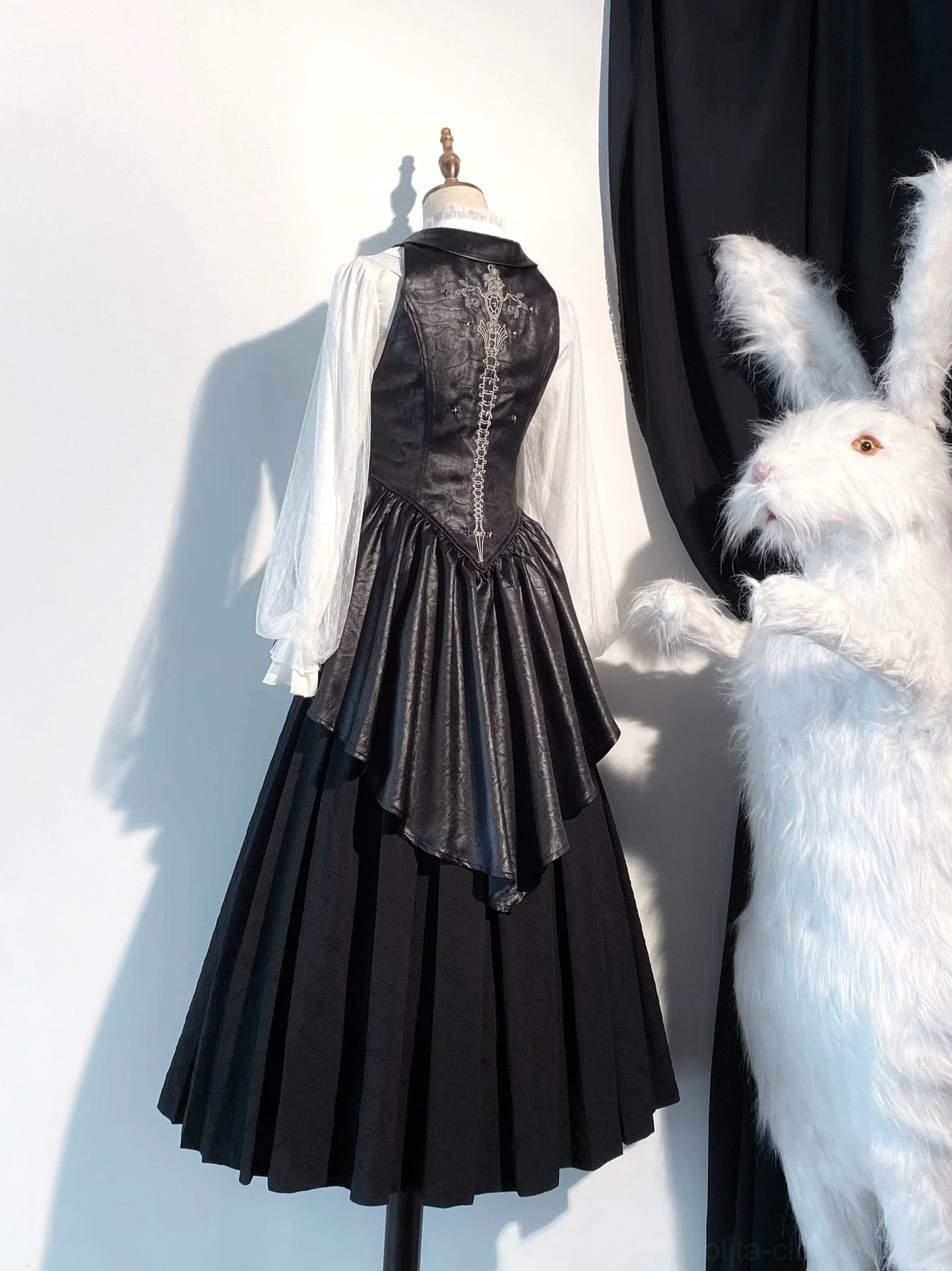 Black gothic lolita vest with high-low pleated skirt, matte leather finish, and sheer white mesh sleeves back view on mannequin
