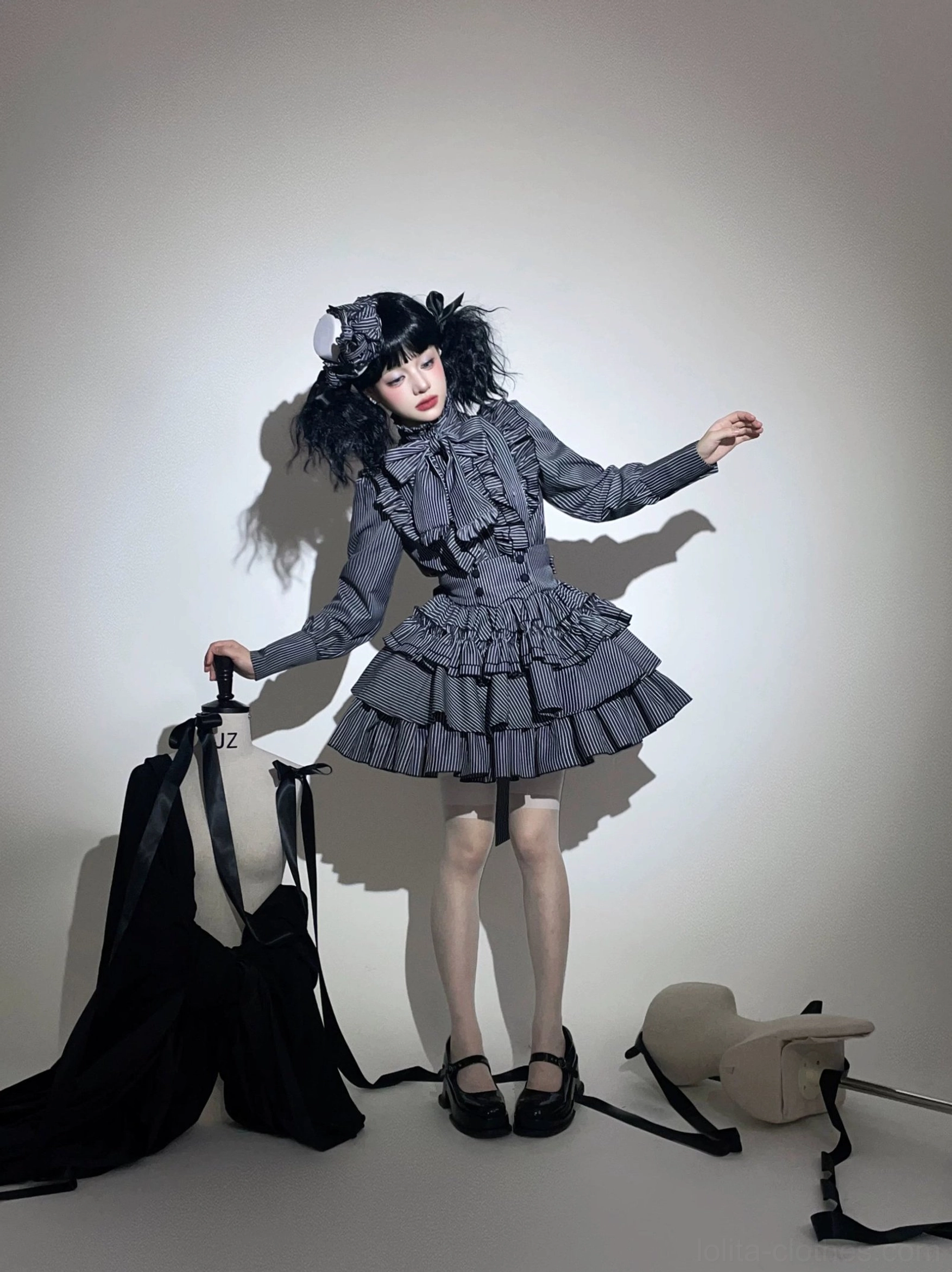 Grey gothic lolita outfit on model in side standing pose showing three-quarter view, displaying belted waist, vertical stripe pattern, and ruffled mini skirt silhouette