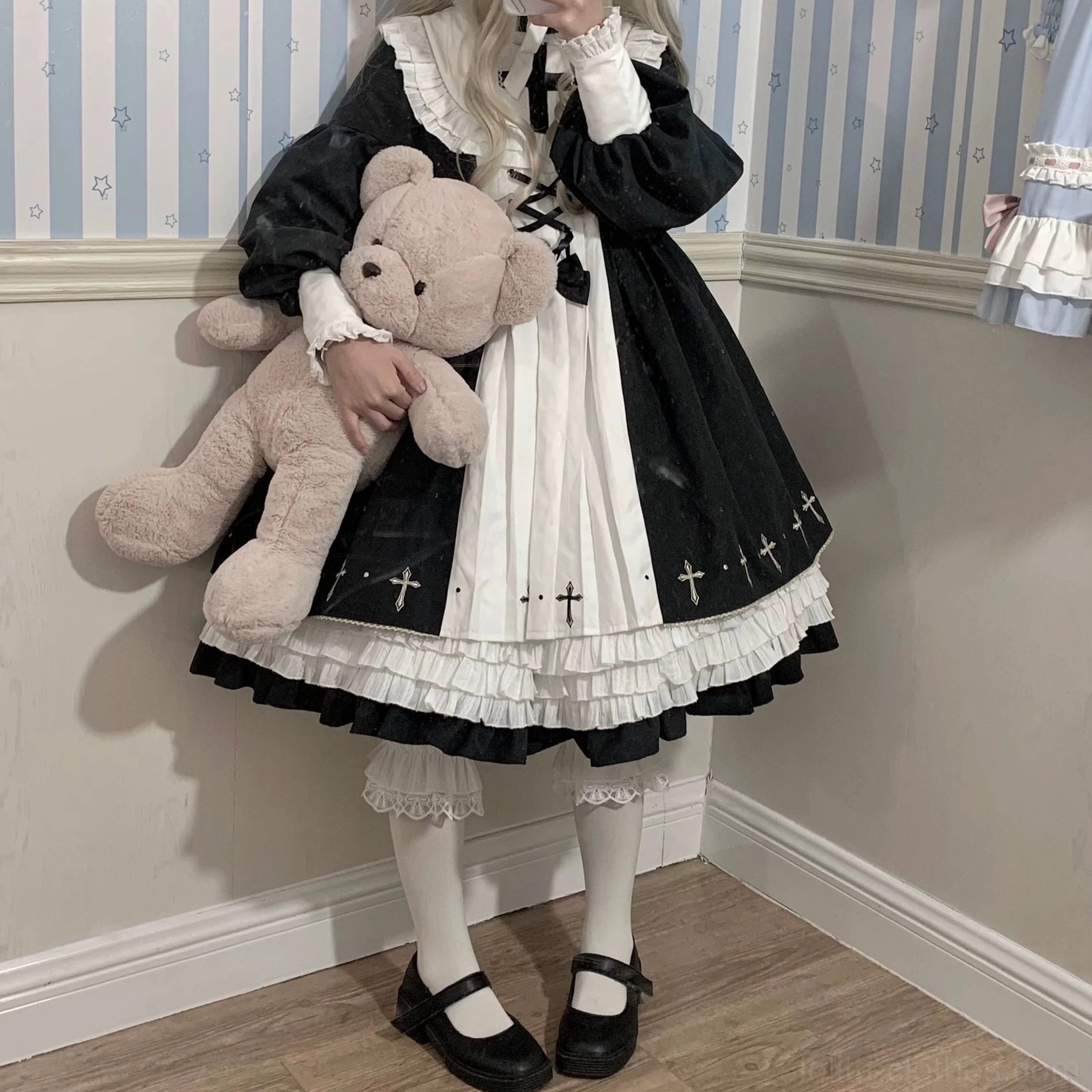 Complete gothic lolita styling with ruffled white lace bloomers visible under cross-print dress white stockings black mary jane shoes and teddy bear prop side standing view