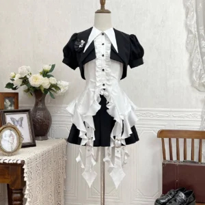 Black and white gothic lolita outfit displayed on dress form showing cropped puff-sleeve jacket, pointed collar shirt, and pleated skirt with ruffled apron in retro indoor setting