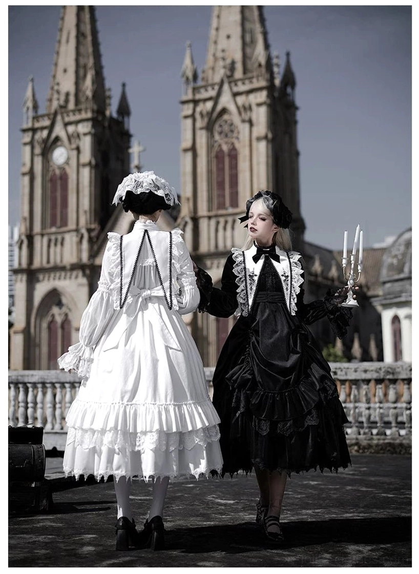 Back three-quarter view of black and white velvet gothic lolita OP dresses with full ruffled midi skirts, cross collar trim details and candelabra prop at cathedral outdoor venue