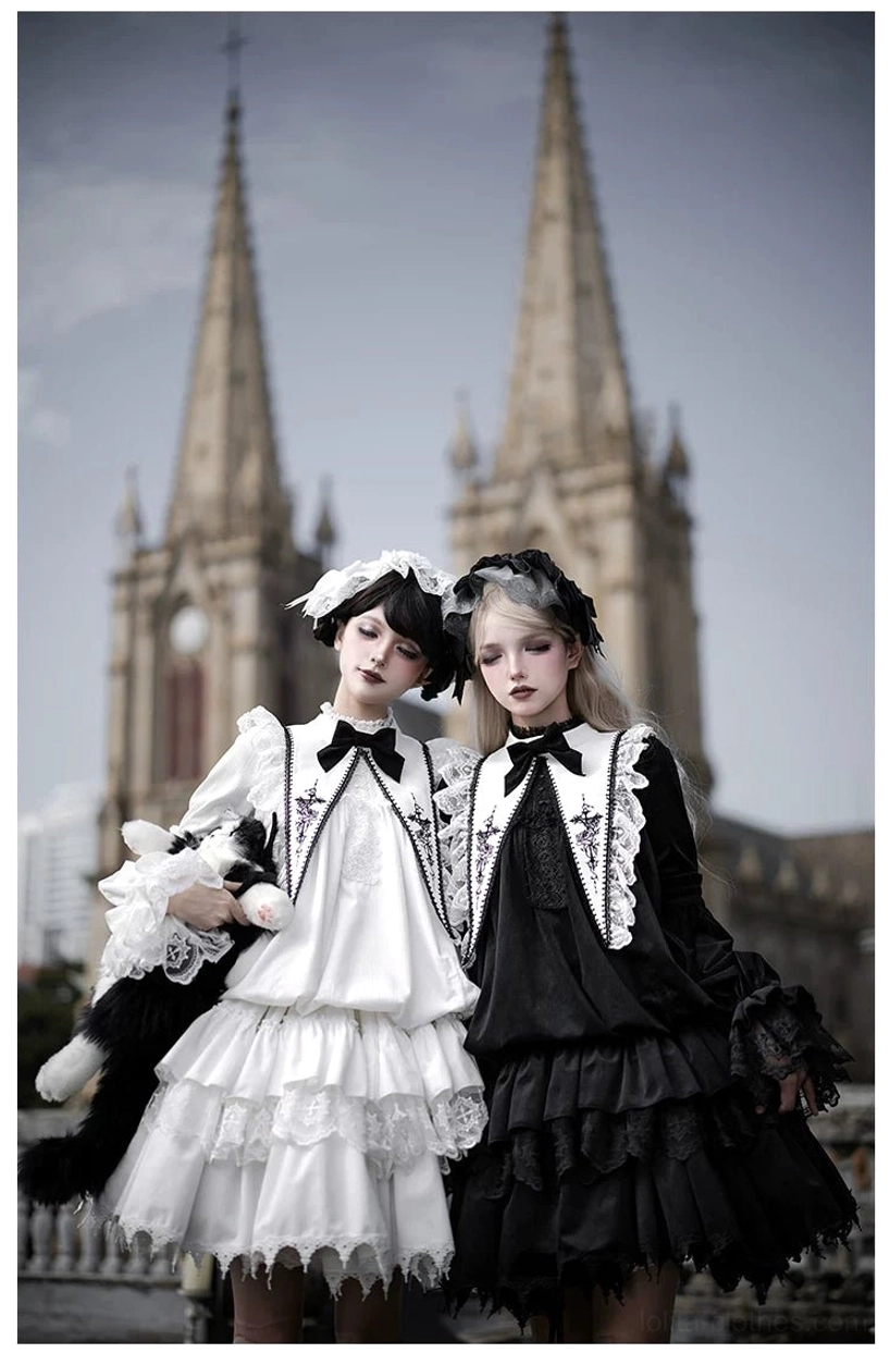 Close-up front view of black and white velvet gothic lolita dresses with matching ruffled tiered skirts, lace-trimmed collars with bow ties and stuffed cat plush props in cathedral setting