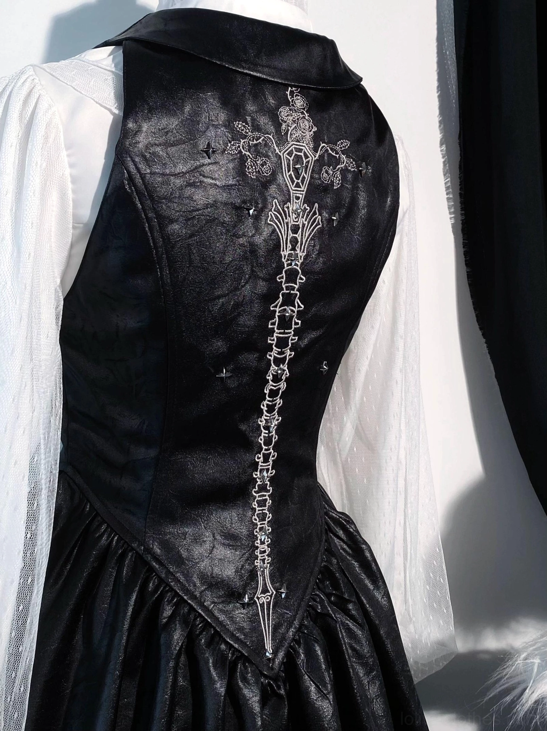 Close-up back detail of gothic lolita waistcoat showing intricate spine and bone-sword silver embroidery on black acetate satin, tailored slim fit construction