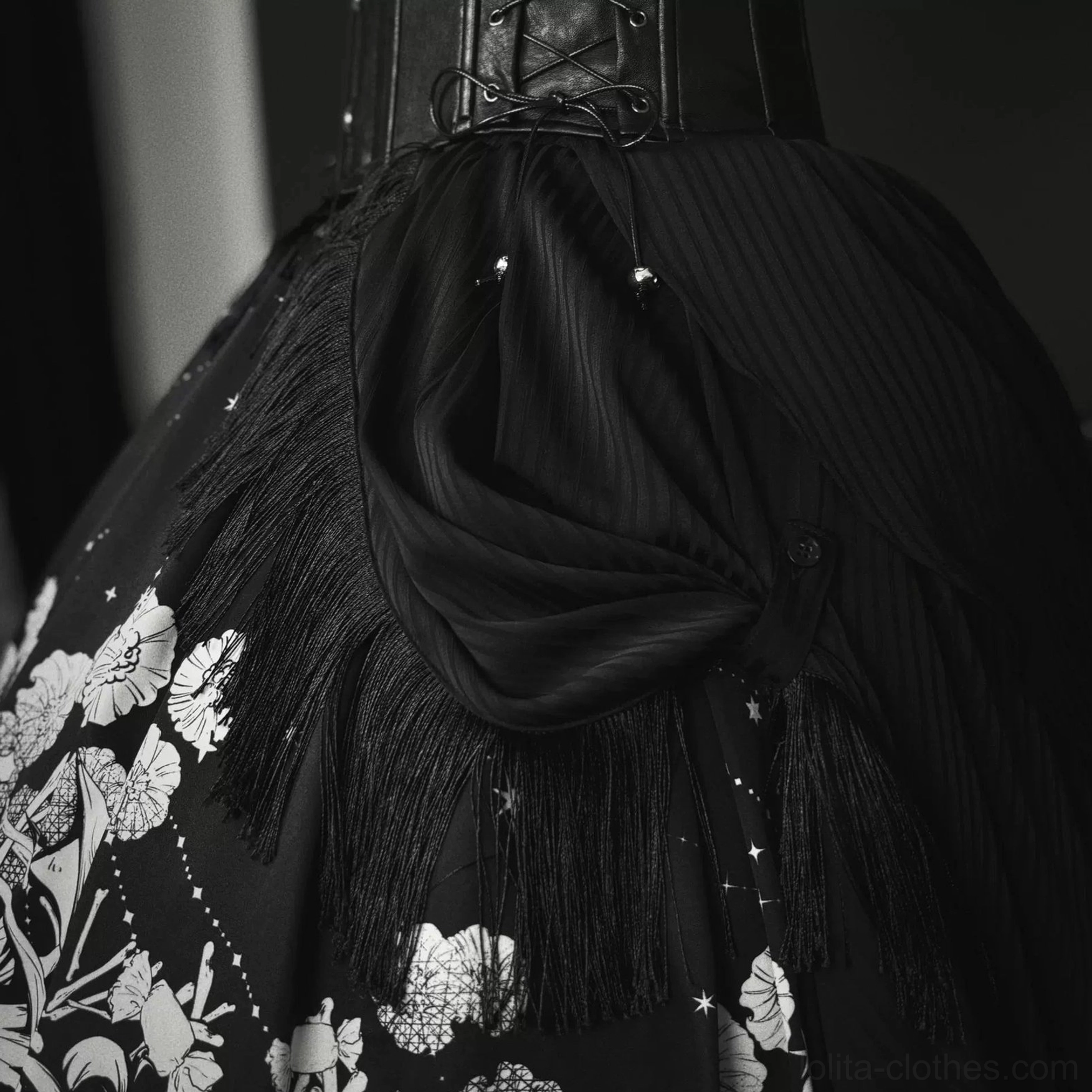 Lower Gothic Lolita outfit detail showing black tassel fringe skirt draped fabric and floral monochrome print coordinating with waist corset