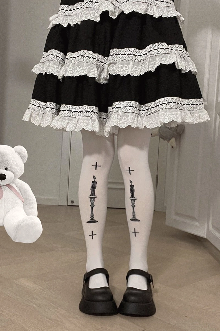 Full standing lower-body view of Gothic Lolita white velvet pantyhose with black cross and candle prints worn with multi-layer lace-trimmed skirt and Mary Jane shoes