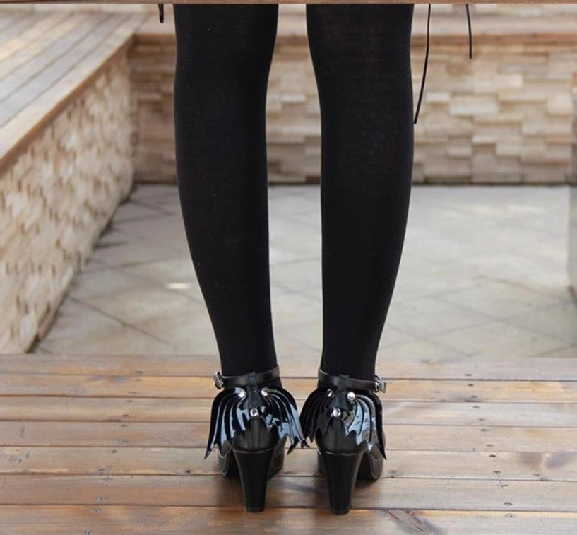 Back on-foot wearing view of Gothic Lolita winged high heel shoes with block heel design, model in black tights, detachable wing charms visible, outdoor terrace landscape