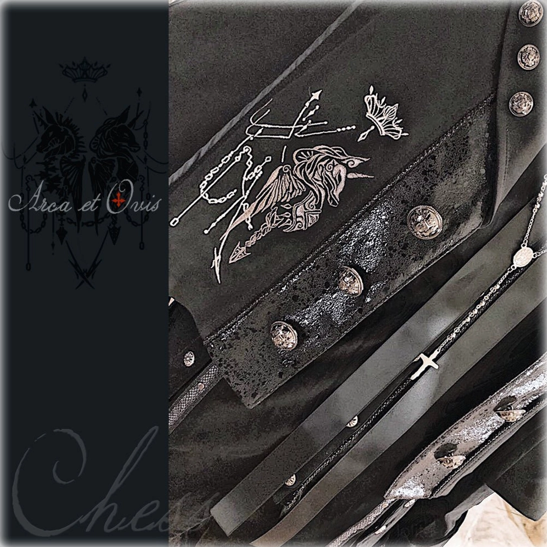 Flat lay product detail showcase of Gothic Ouji cape featuring silver knight and crown embroidery, metal stud fasteners, cross pendant strap details, and dark black color scheme close-up