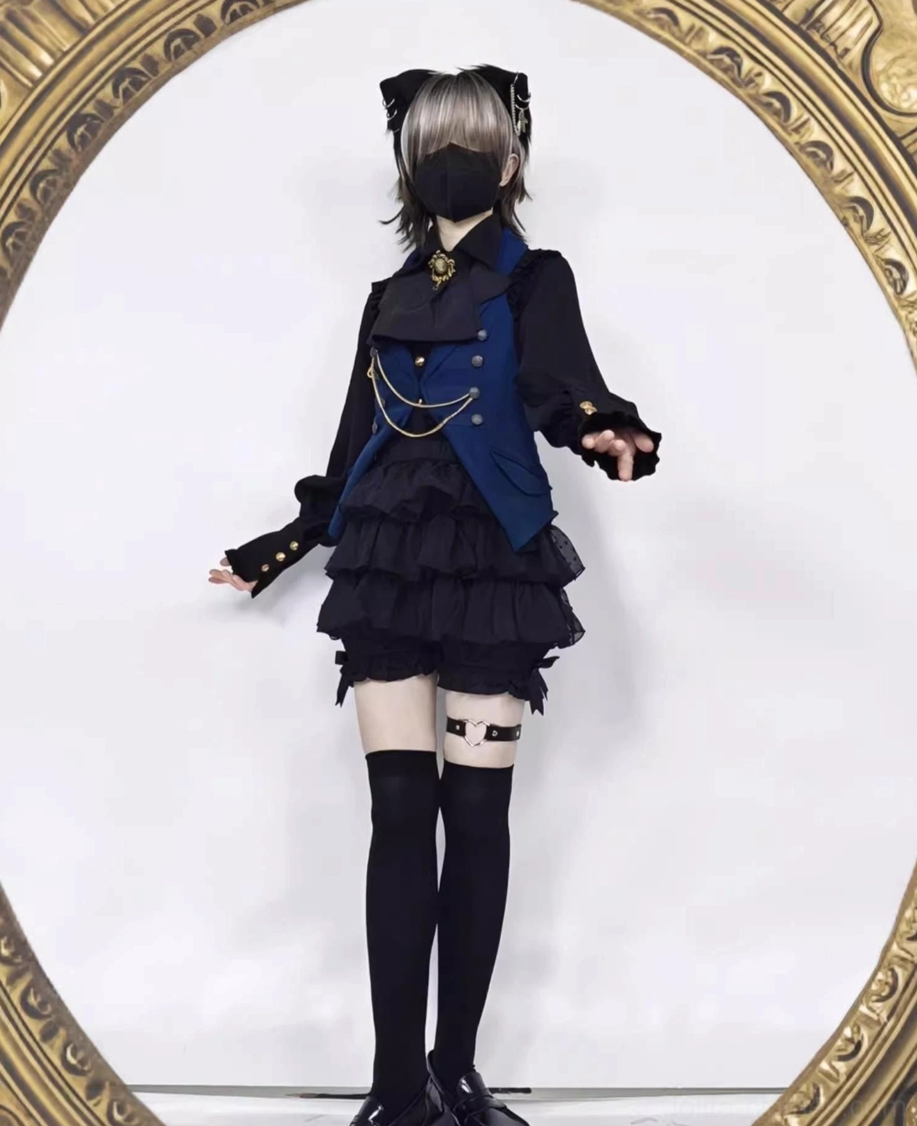 Male model wearing gothic ouji lolita coordinate set with navy gold-chain vest black blouse thigh-high socks tiered ruffle bloomers and full gothic prince styling with cat ear accessories