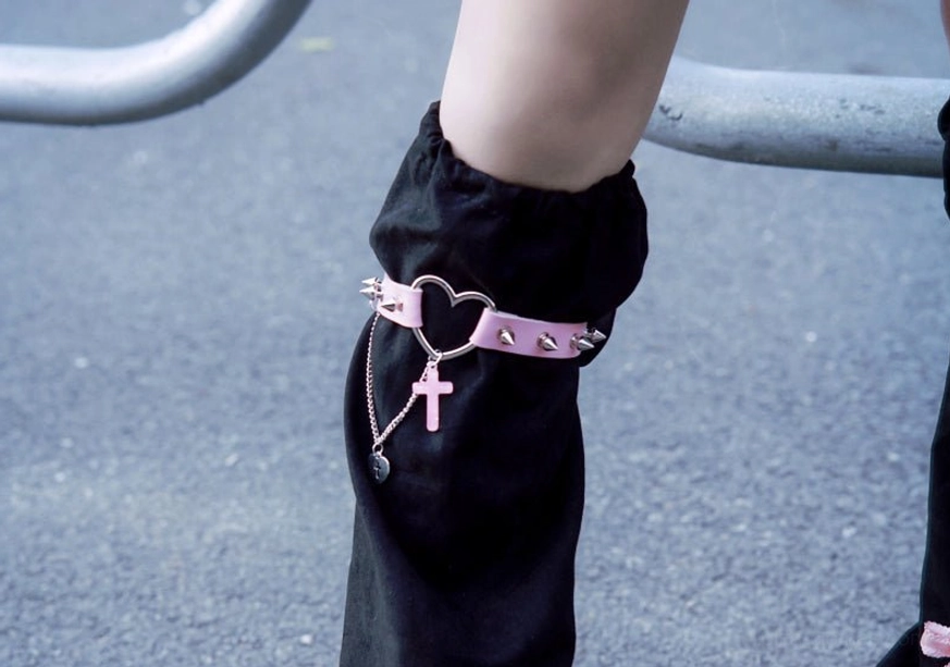 Close-up side detail view of gothic suede leg warmer showing pink heart cross strap metal chain pendant black suede fabric texture and craftsmanship