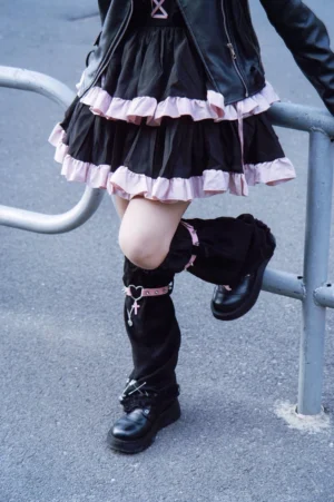 Black and pink gothic suede leg warmers with heart cross charm details and pink rivet straps worn outdoors by model in black pink lolita outfit