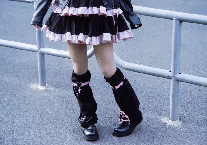 Low front partial dual-leg view of gothic suede leg warmers with minimal pink strap decoration subtle metal details worn in outdoor street lolita coord