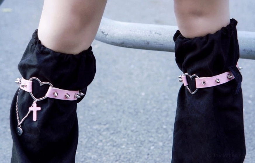 Close-up side dual-leg view of gothic suede leg warmers displaying studded pink leather straps cross charm pendants metal accents lolita aesthetic