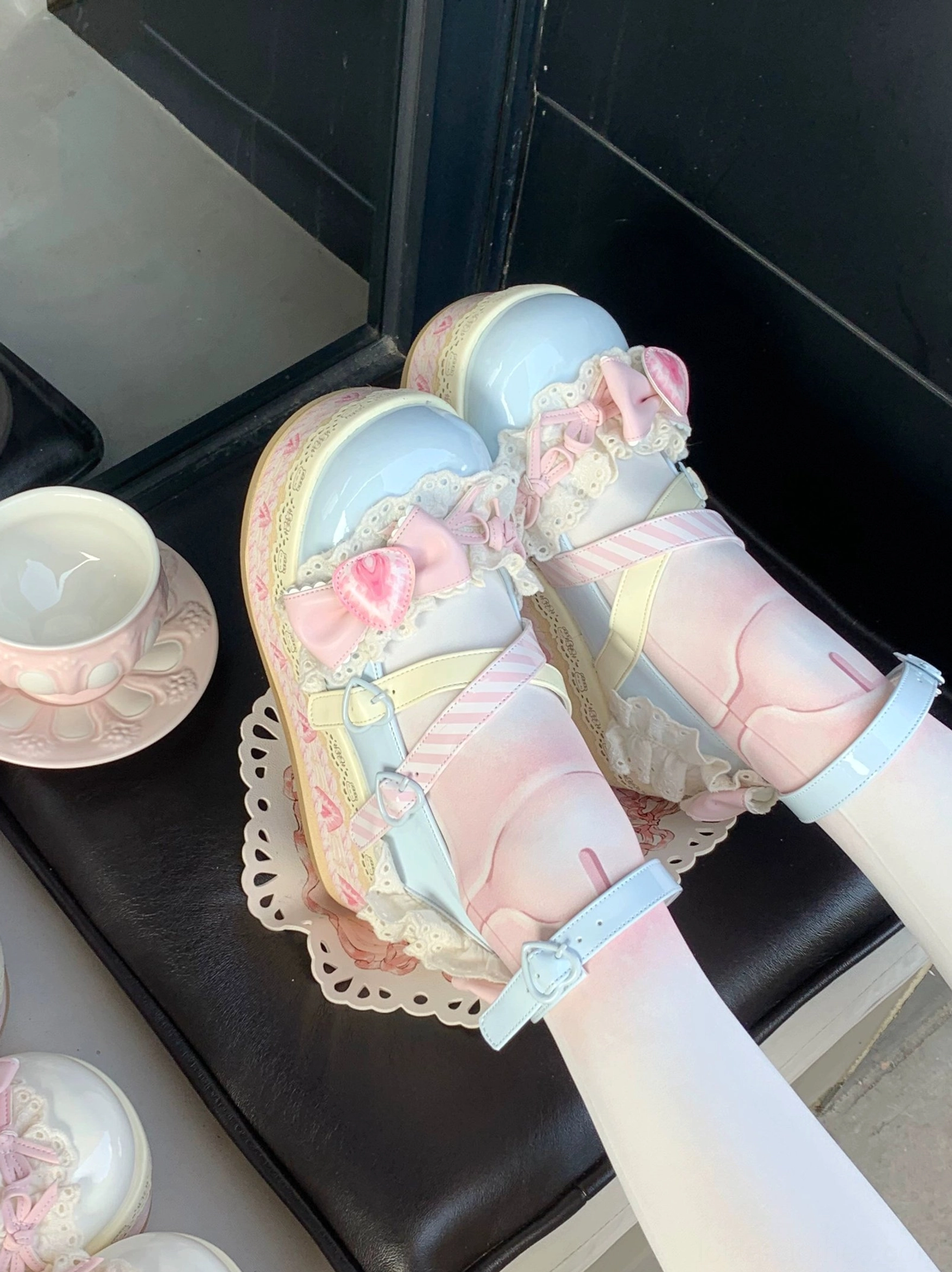 Gradient sweet lolita platform shoes side view on foot with pink-blue upper and heart flower decor worn with gradient white stockings on black leather chair