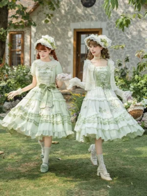 Pair of models in matching green grape embroidered lolita dresses with shirred bodices walking on sunlit lawn wearing coordinating gloves and bonnets side angle