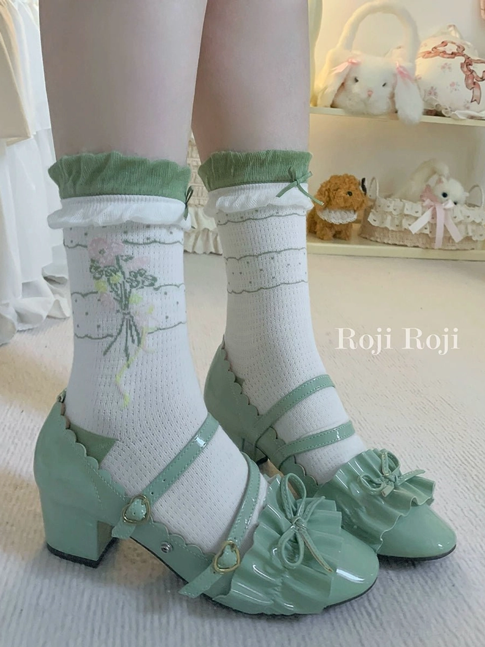 Green scalloped Mary Jane shoes coordinated with matching sage green ruffled cuff ankle socks featuring white base floral and stripe print front angle low perspective