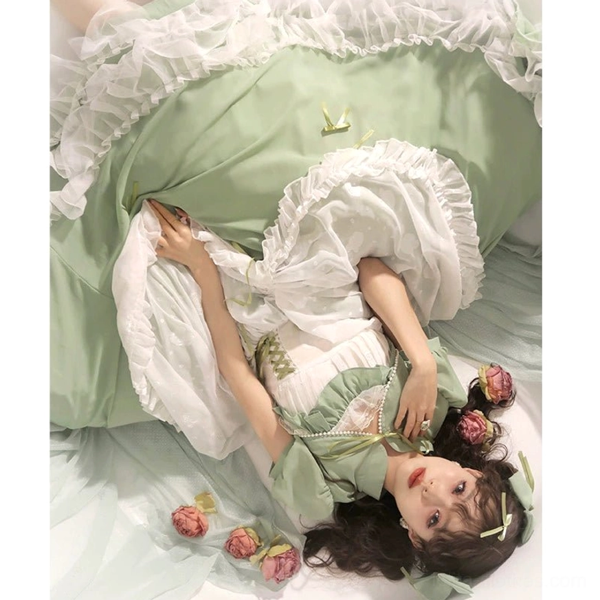 Close-up overhead view of sage green lolita wedding JSK dress showing pearl bodice decoration, layered white ruffled trims, satin fabric texture, and intricate hand-sewn details