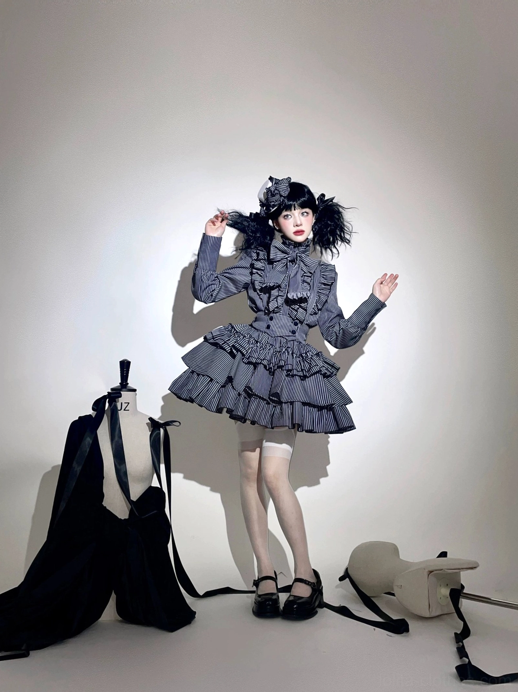 Grey gothic lolita striped suit on playful model in three-quarter front pose, featuring tiered ruffled skirt, bow neck detail, and long fitted ruffled sleeves