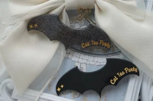 Solid black and transparent glitter black Gothic Lolita bat hair clips displayed on cream chiffon with ornate white frame styling