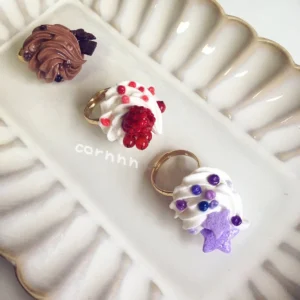 Close flat lay of handmade cream roll dessert adjustable rings with gold-tone bands in chocolate violet and red kawaii Lolita style