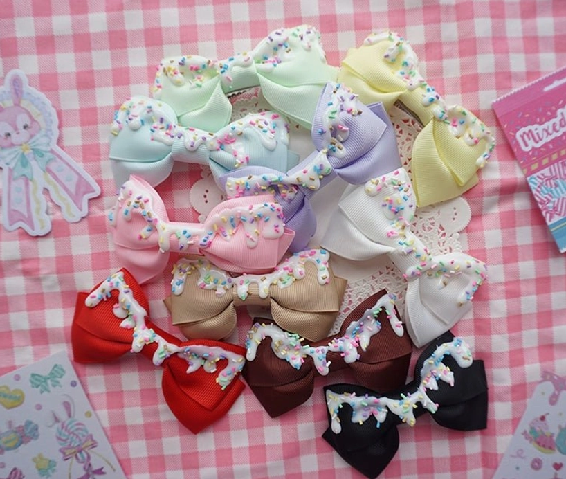 Collection of eight handmade lolita bow hair clips with cream frosting and candy sprinkles decoration displayed flat lay on checkered table
