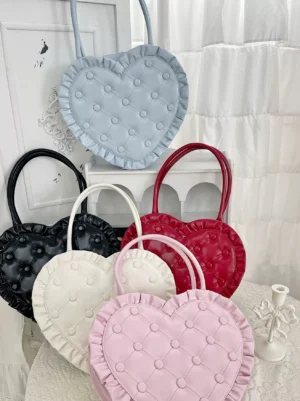 Multiple heart-shaped sweet lolita handbags in various colors displayed overhead flat lay showing quilted buttoned surface and ruffled trim details