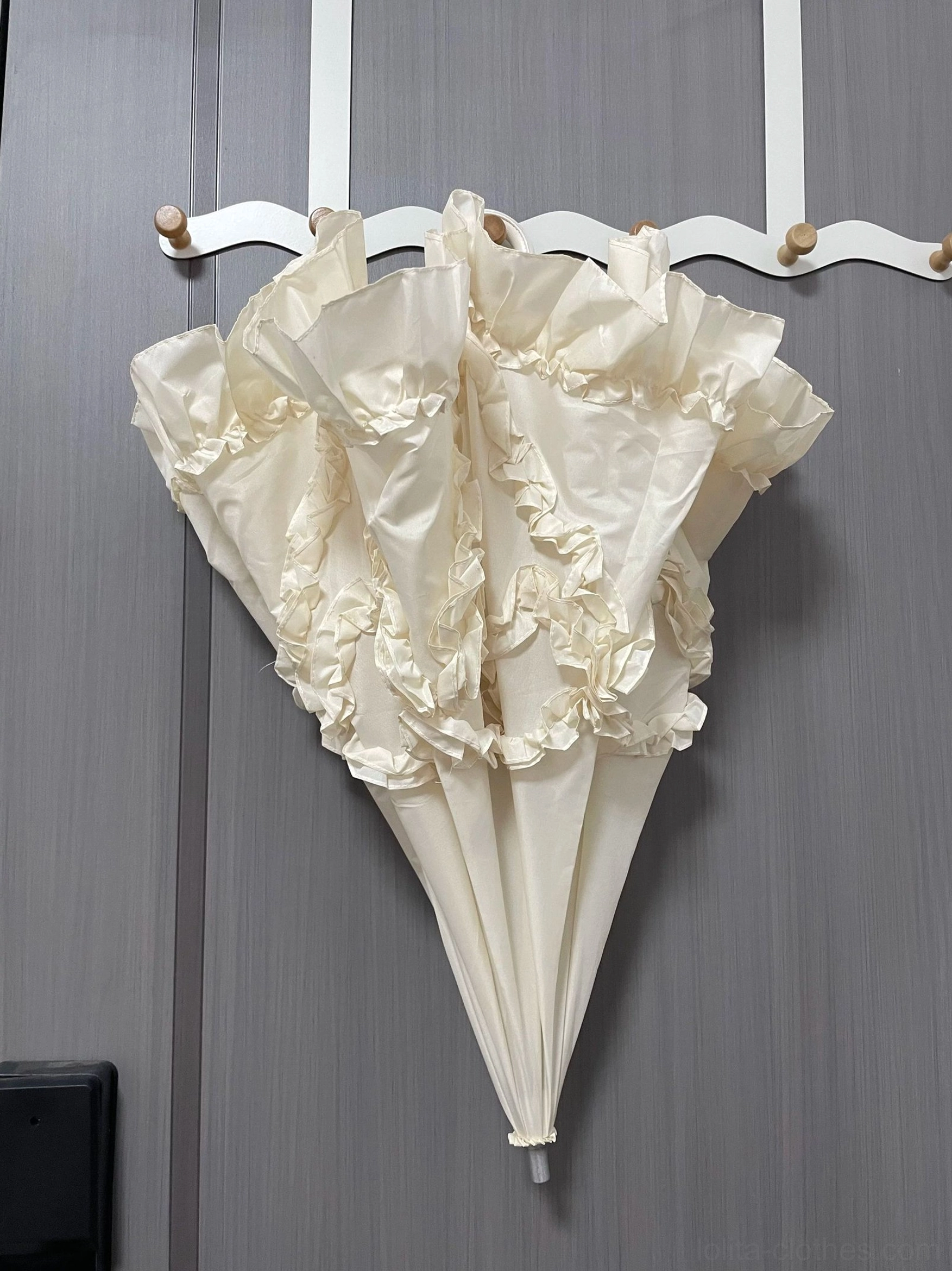 Ivory bow-shaped ruffled Lolita parasol with elegant ruffled canopy edge and simple silhouette on wall hooks, front hanging view showcasing sweet Lolita aesthetic