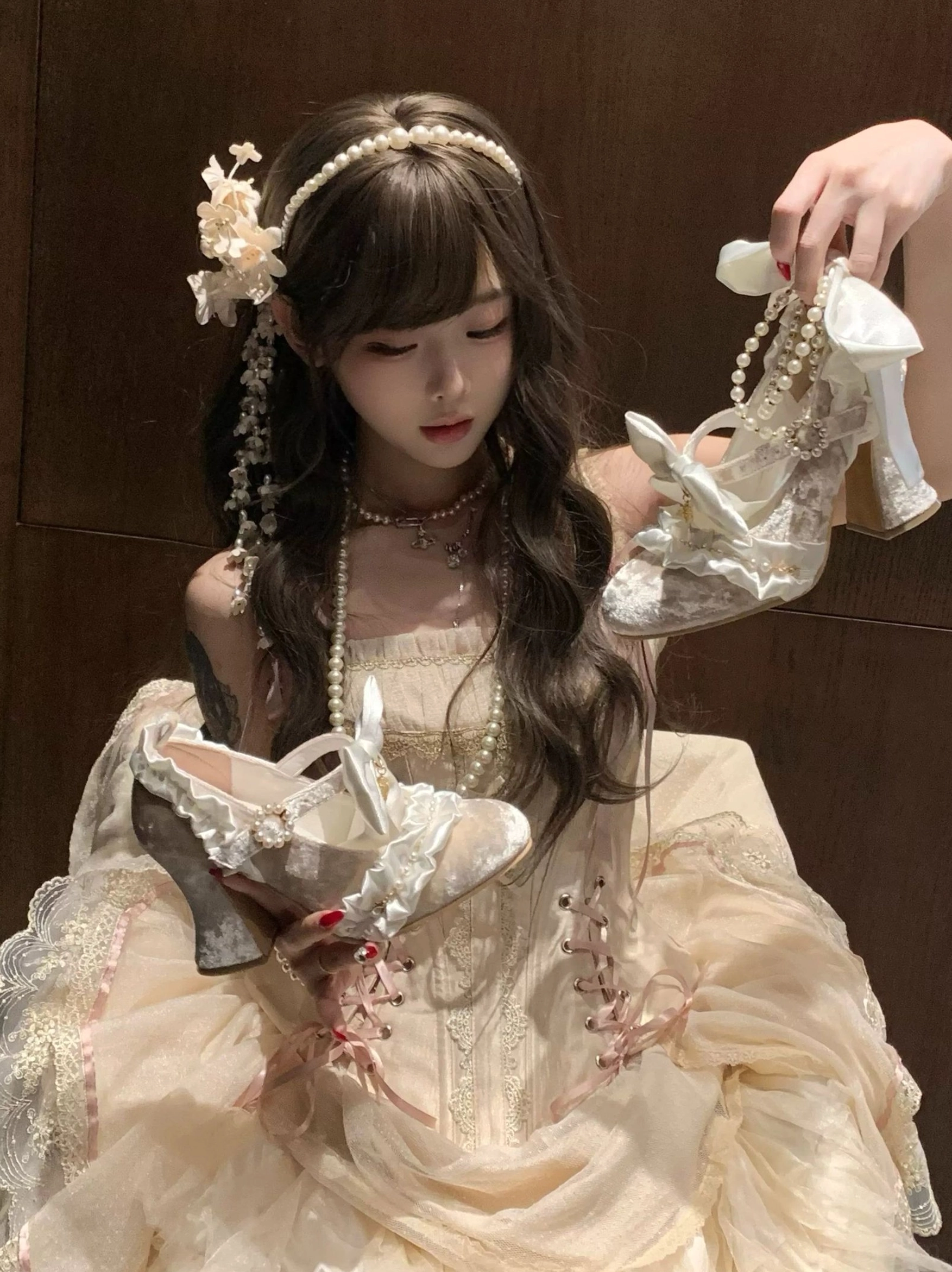 Ivory Classic Lolita block heel shoes with pearl ankle strap and satin bow, model holding shoes with both hands, paired with beige vintage Lolita dress and flower hair ornaments