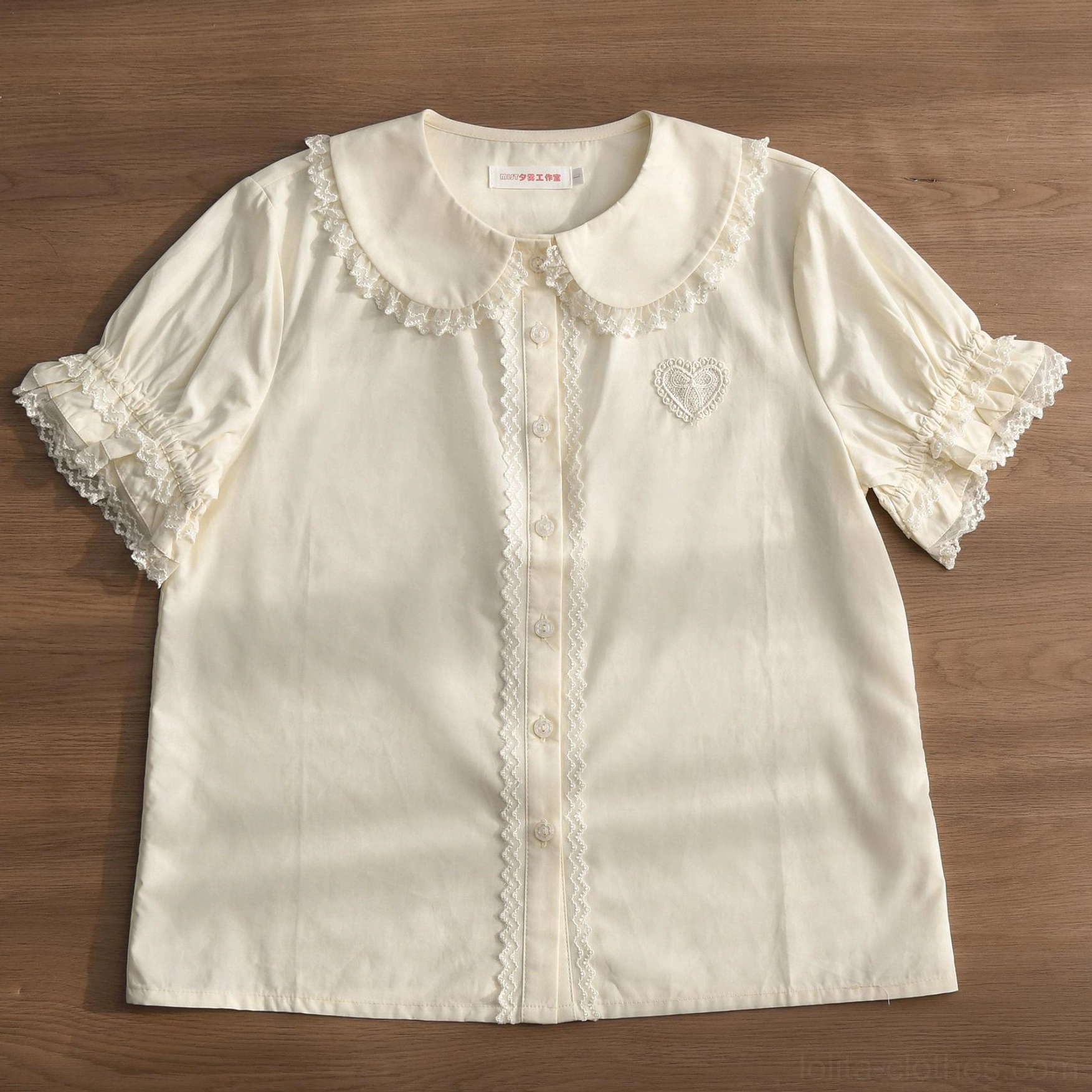Cream white Lolita blouse with lace-trimmed Peter Pan collar and ruffled sleeve cuffs, displayed on wooden background