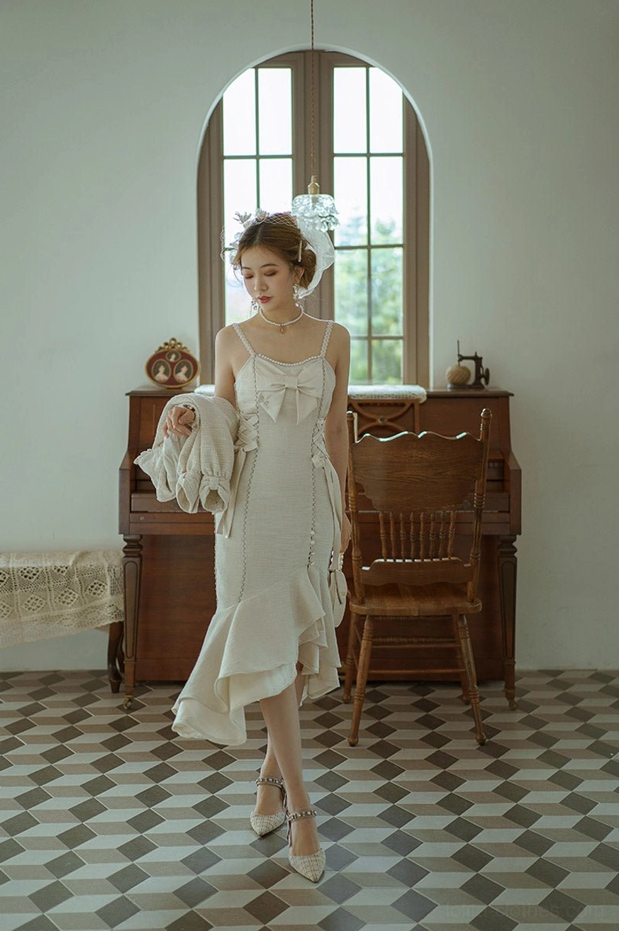 Ivory cream fishtail slip Lolita dress with spaghetti straps, bust bowknot and ruffled fishtail hem in slim midi length, walking pose in retro piano room with checkered floor