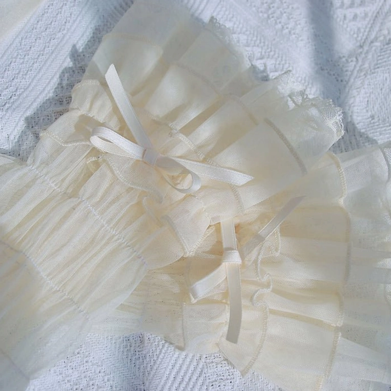 Cream off-white Gothic Lolita arm cuffs with pleated sheer fabric, dual tiered ruffles and white satin ribbon bows on grey textured fabric background