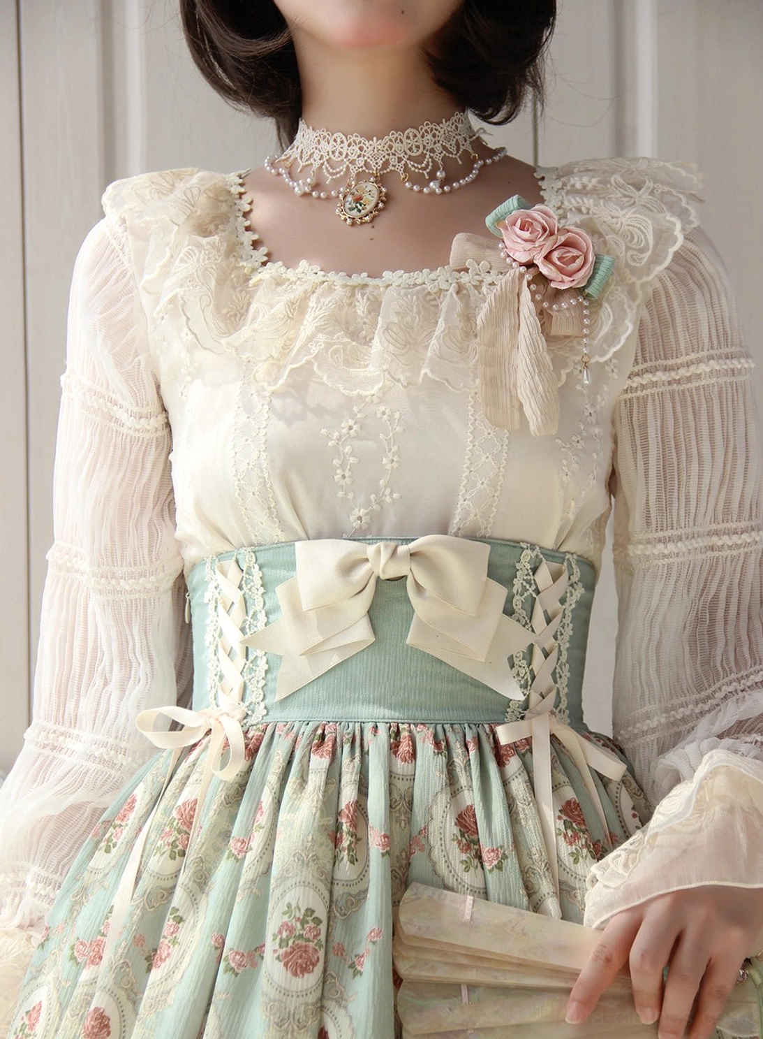 Close-up detail of square neckline with ruffled lace trim, pearl choker, and pink rose brooch on ivory Lolita blouse