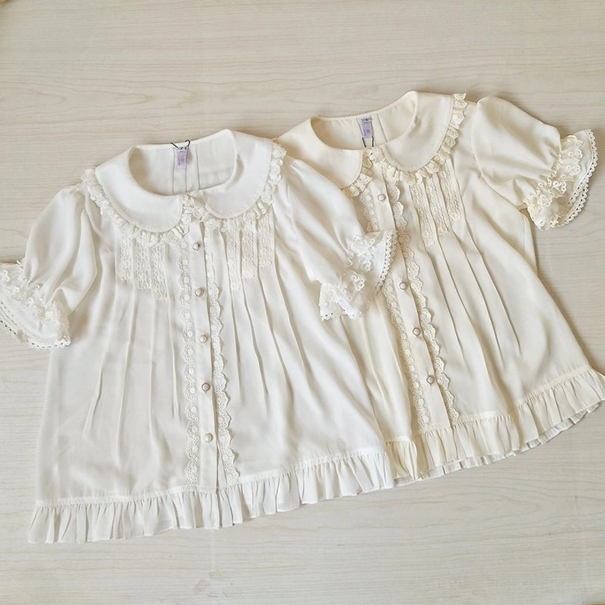 Two matching ivory sweet lolita Peter Pan collar blouses flat lay top-down view on wooden surface showing ruffled hem and design details