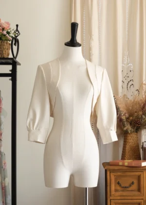 Vintage ivory lolita bolero with three-quarter bishop sleeves displayed on dress mannequin in retro home studio setting
