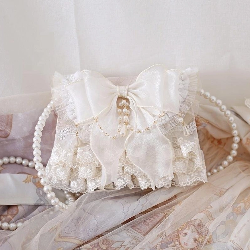 Elegant ivory lolita crossbody handbag with double-layered bow and pearl pendant on silky lolita dress fabric side view