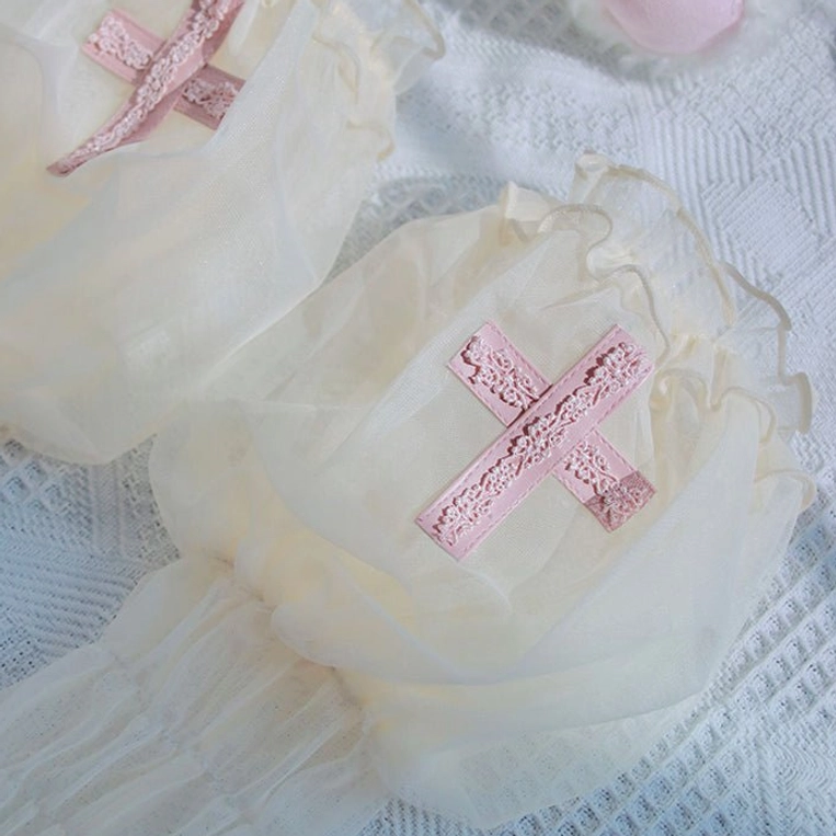 Cream off-white Gothic Lolita arm cuffs with pink lace cross embroidery details, sheer mesh and ruffled frill edges on blue textured fabric backdrop