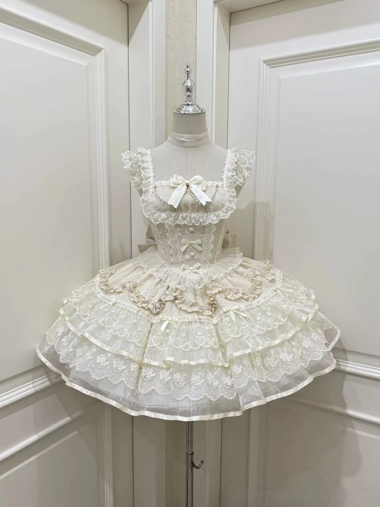 Front display of ivory sweet lolita JSK dress showcasing embroidered bodice details, small satin bust bow, and multi-tiered lace petal-style ruffled skirt on dress form