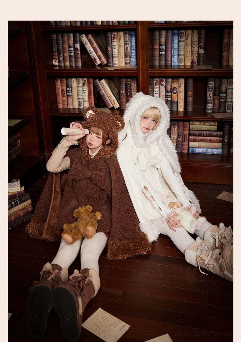 Bear themed and rabbit themed winter lolita capes with fuzzy ear hoods and plush decorative elements displayed by two models sitting on wooden library floor wearing coordinating snow boots